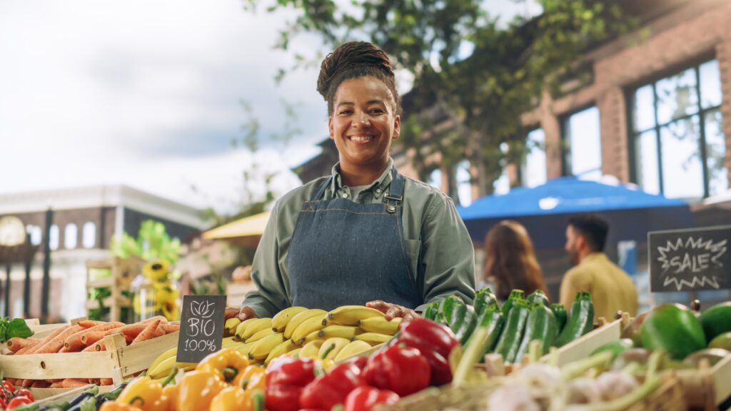 small business owner at her fruit stand with veggies in the forefront smiling into the camer