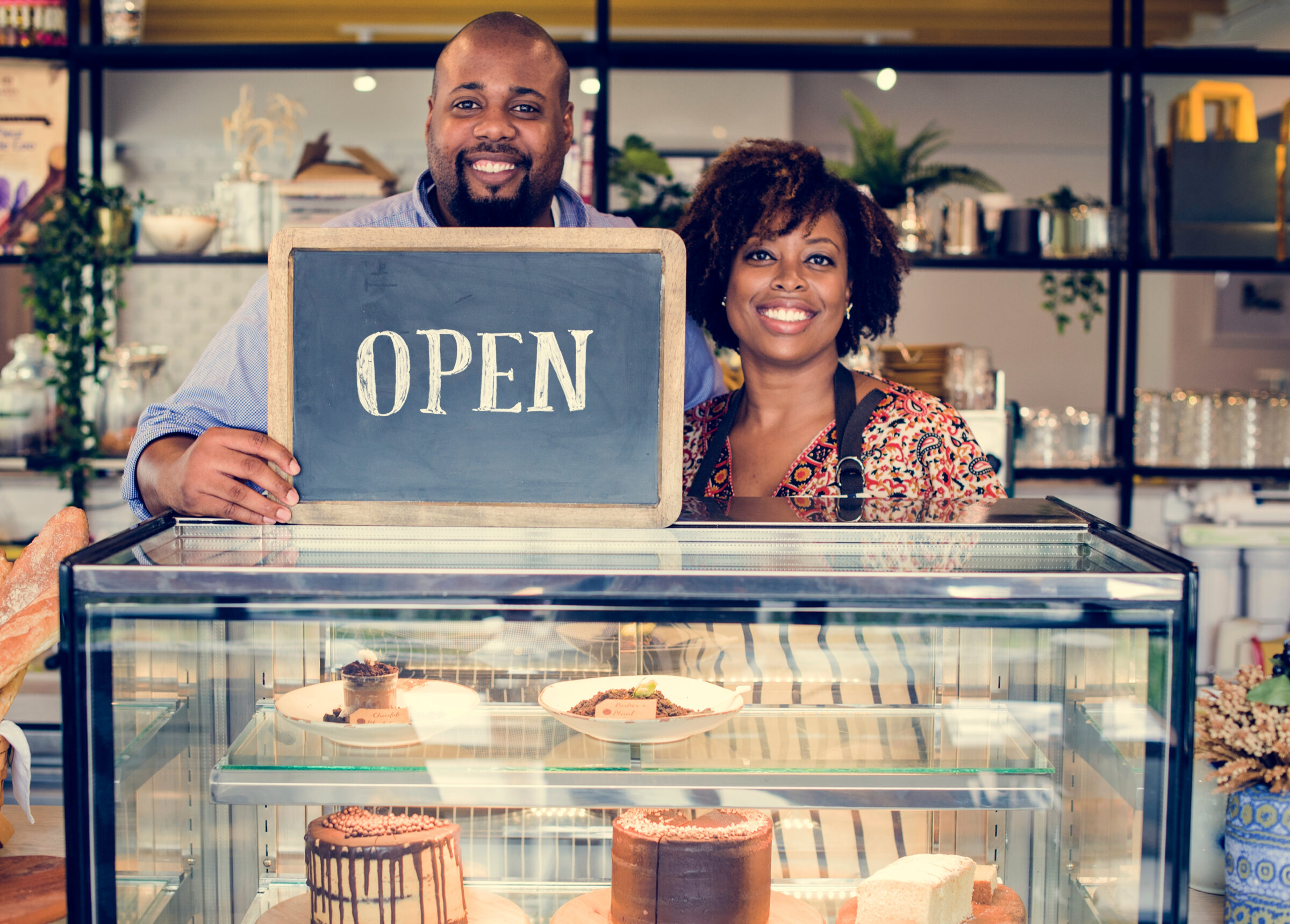 black couple holding open sign after they open a bakery